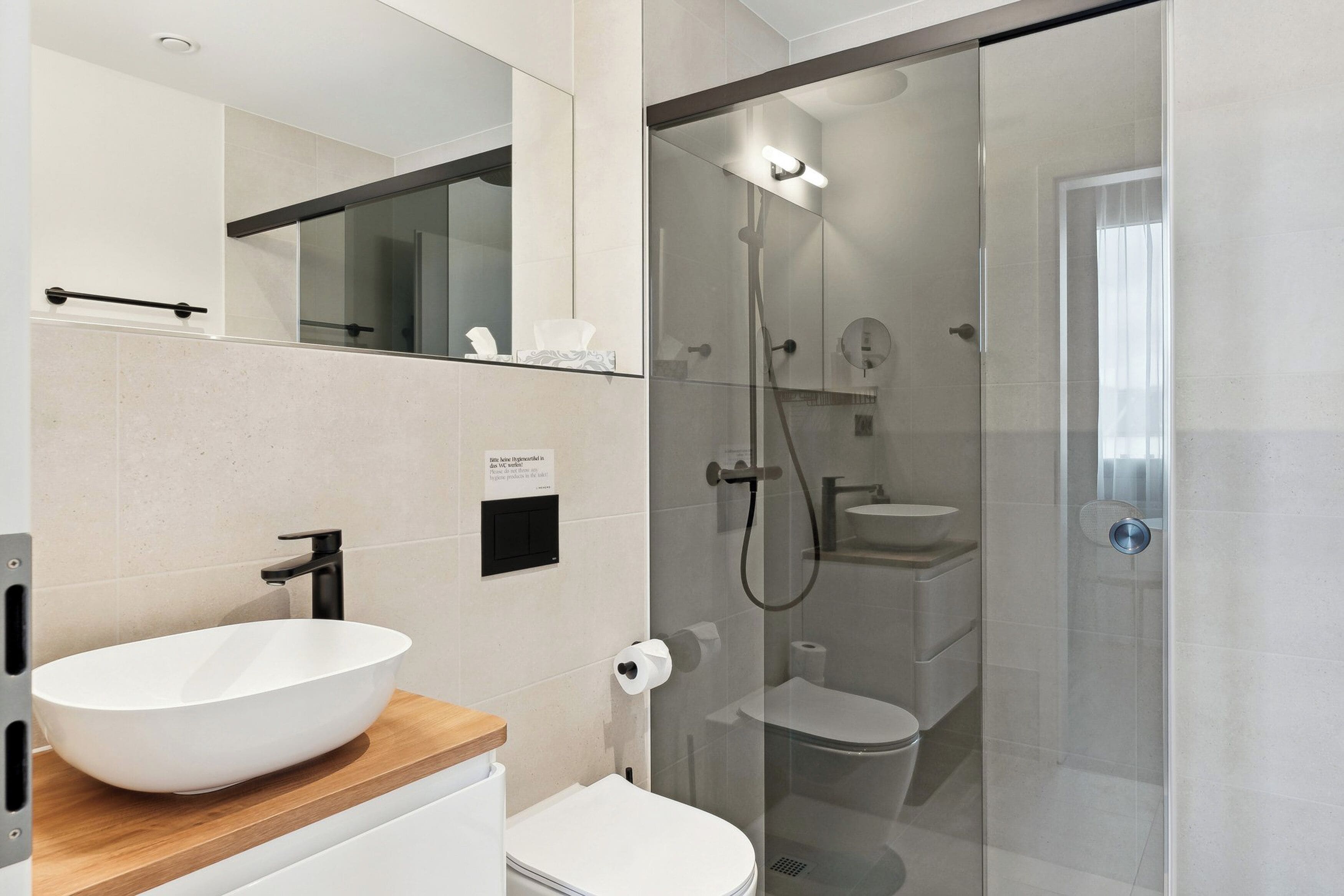 A modern bathroom with a white sink, toilet, and glass-enclosed shower.