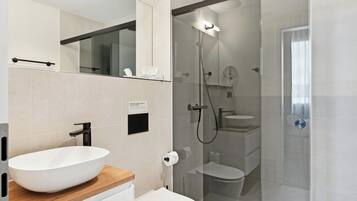 A modern bathroom with a white sink, toilet, and glass-enclosed shower.