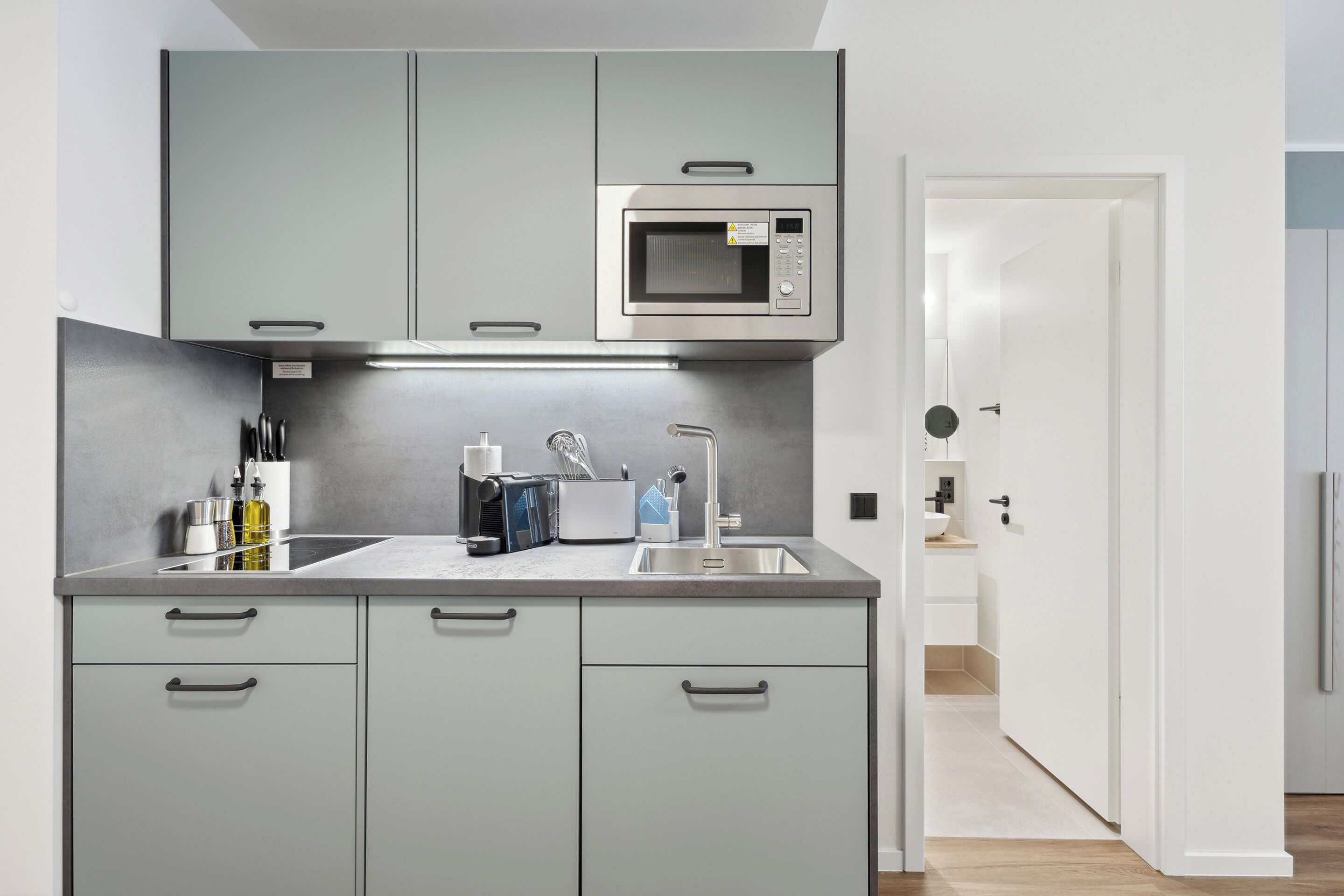 A modern kitchen with grey cabinets, a stainless steel microwave, and a sink.