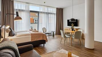 A modern hotel room with a bed, a sofa, a dining area, and a TV.
