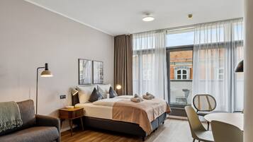 Una camera da letto moderna con un letto, comodini, una scrivania e una sedia. Sono presenti tende, una finestra e vista sugli edifici.