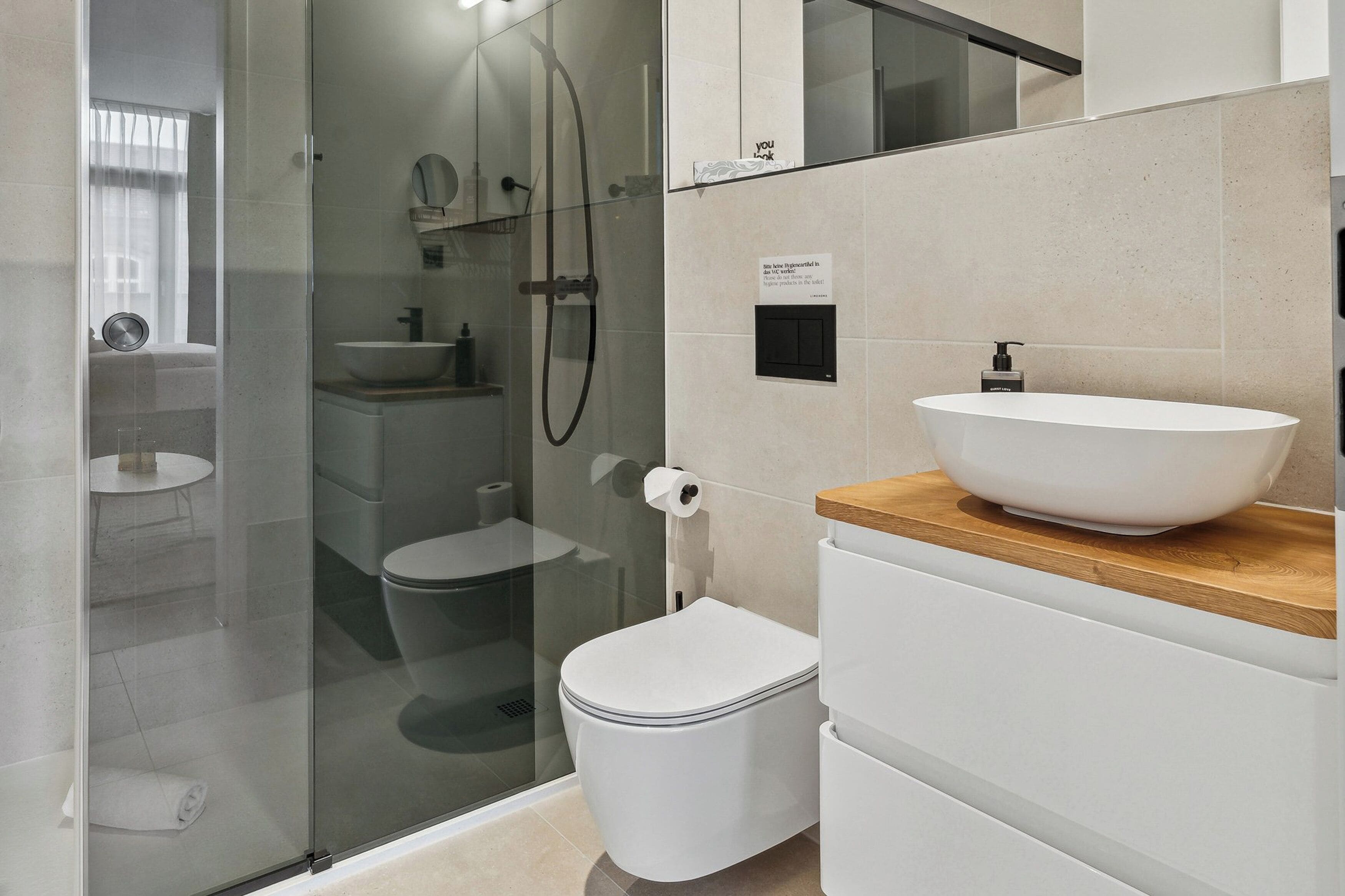 A modern bathroom with a glass-enclosed shower, a white toilet, a wooden vanity with a white sink, and a small round table.