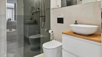 A modern bathroom with a glass-enclosed shower, a white toilet, a wooden vanity with a white sink, and a small round table.