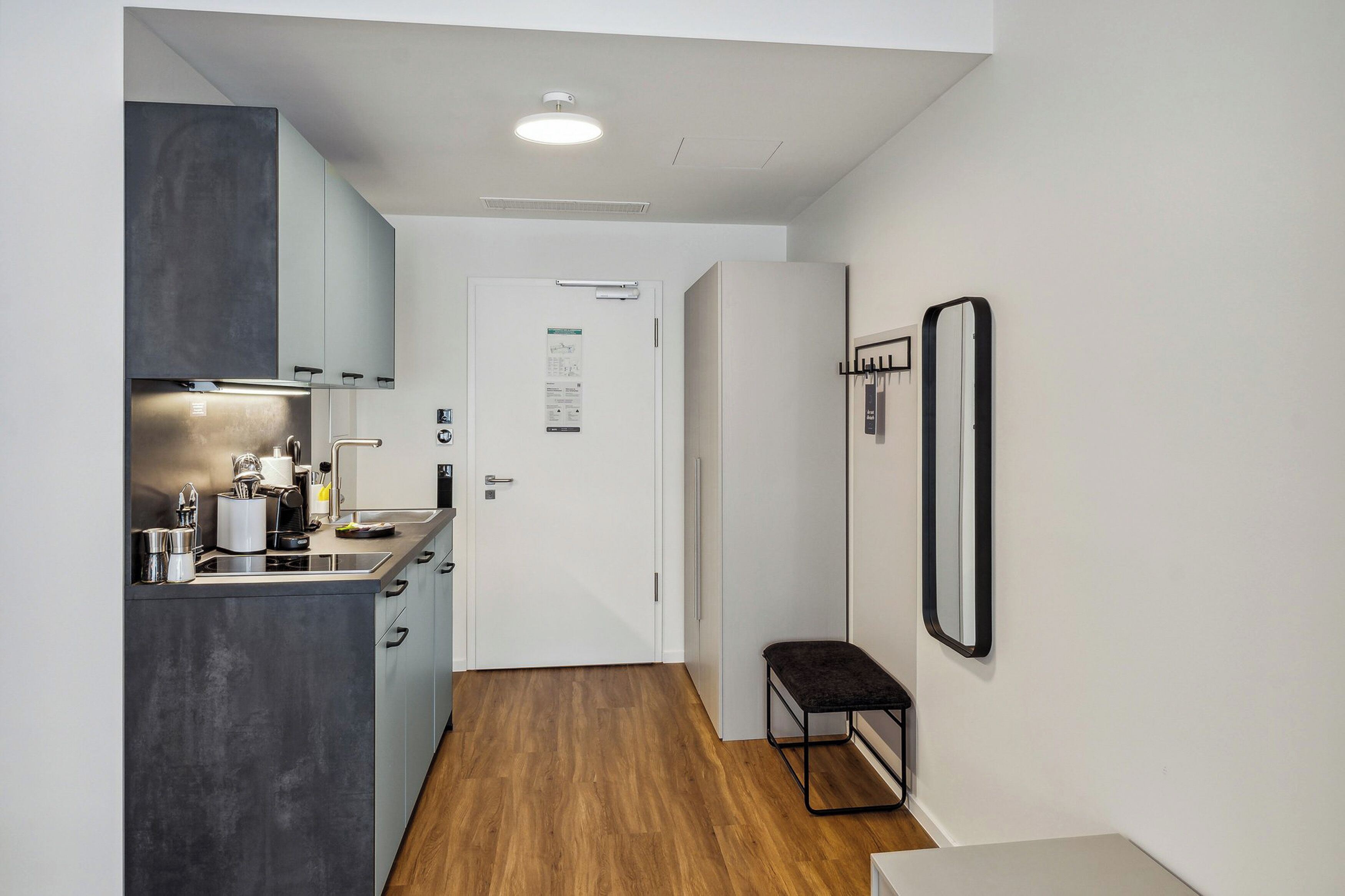 Une cuisine compacte dotée d’appareils électroménagers modernes, d’un banc et d’une porte sur laquelle est affiché un avis.