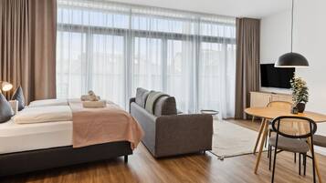 A modern hotel room with a bed, sofa, dining table, and TV.