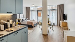 Habitació d'hotel moderna amb cuina, un llit, una taula de dinar i un televisor.