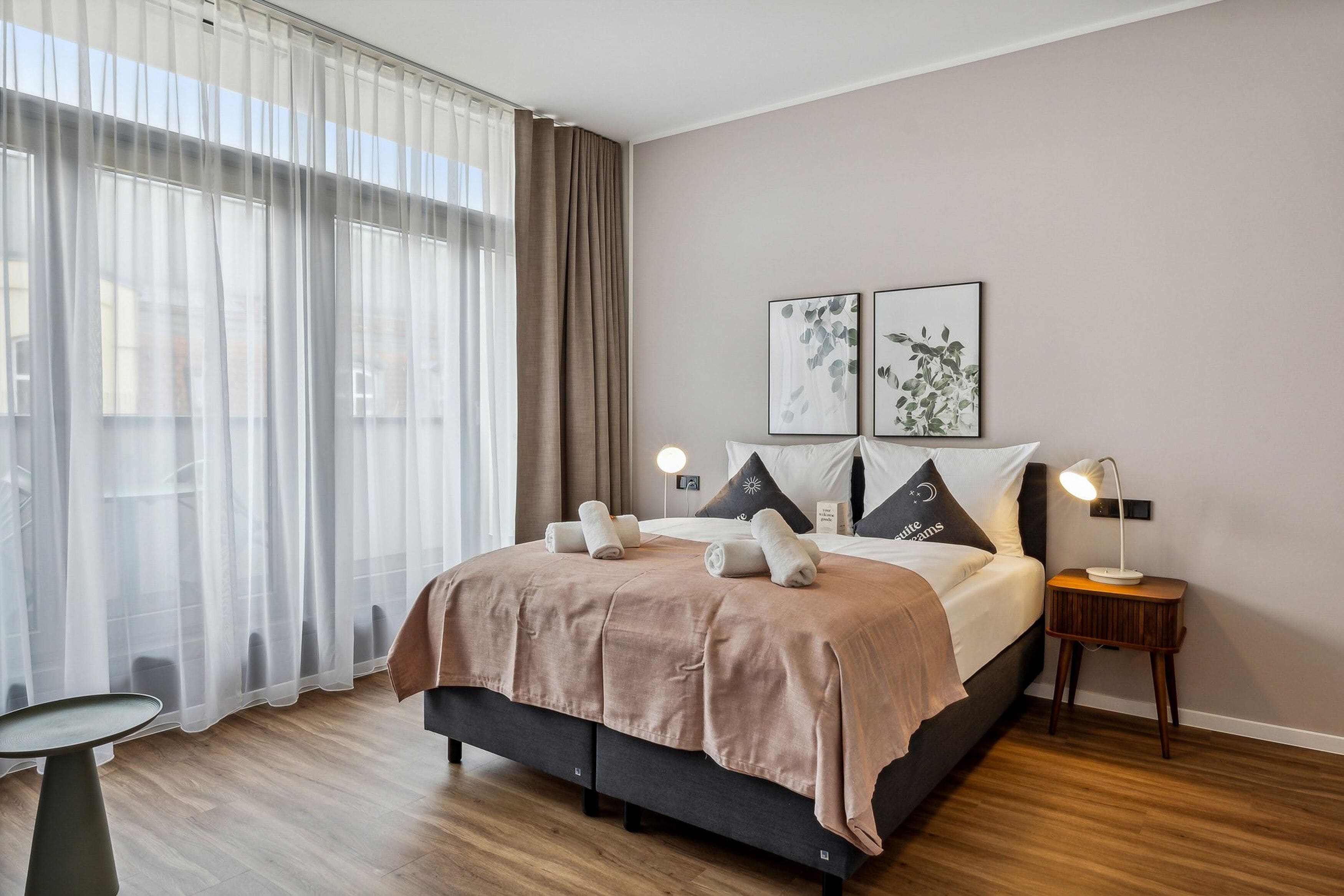 A neatly made bed with a pink blanket, two pillows, and a bedside lamp.
