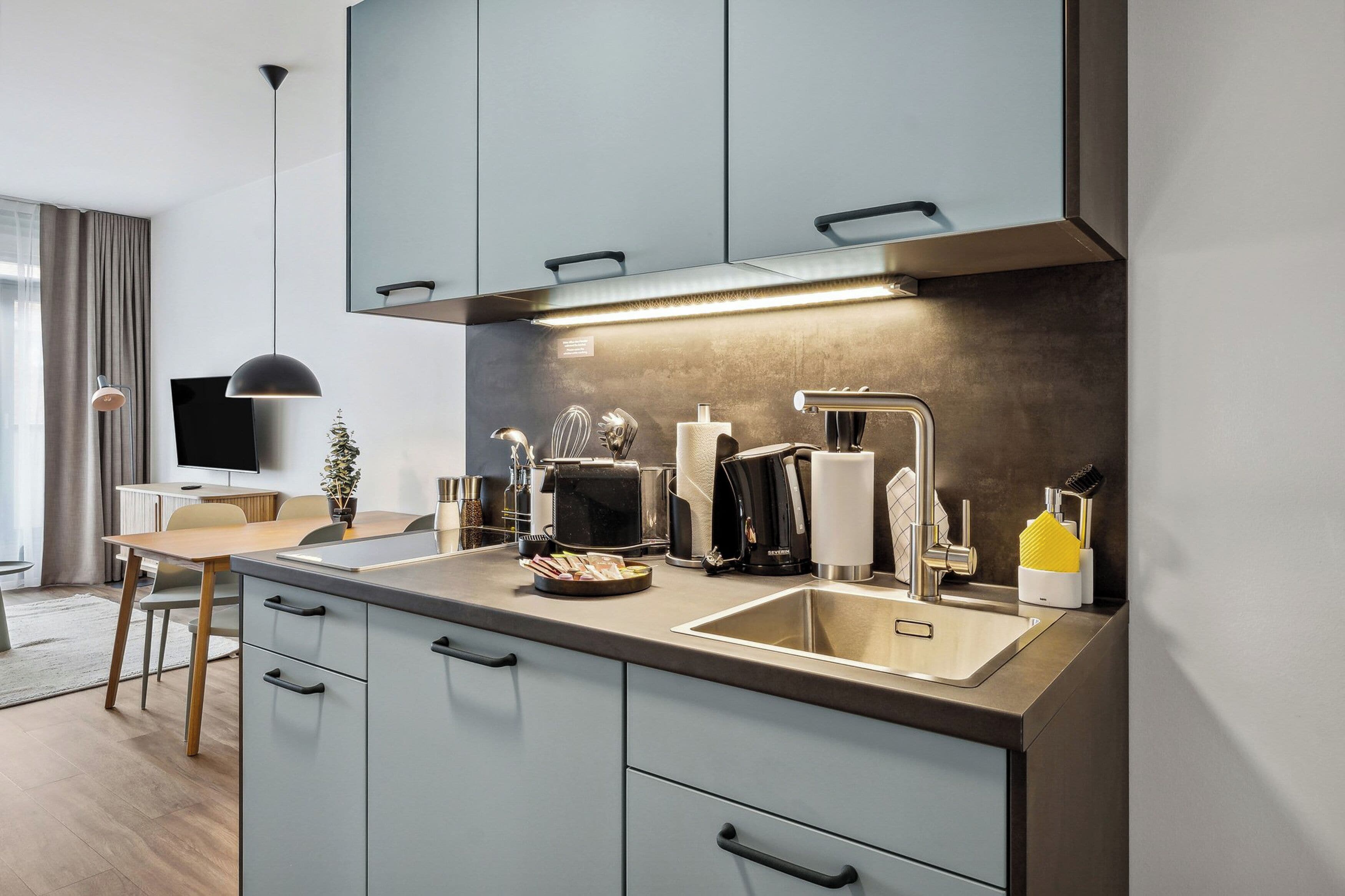 A modern kitchen with a built-in oven, microwave, and coffee maker. There is a sink with a faucet and a countertop with various kitchen items.