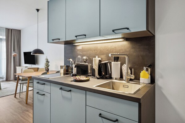 A modern kitchen with a built-in oven, microwave, and coffee maker. There is a sink with a faucet and a countertop with various kitchen items. - Limehome Zwickau Magazinstr. (Zwickau)