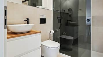 A modern bathroom with a large white vessel sink, a toilet, and a glass-enclosed shower area.