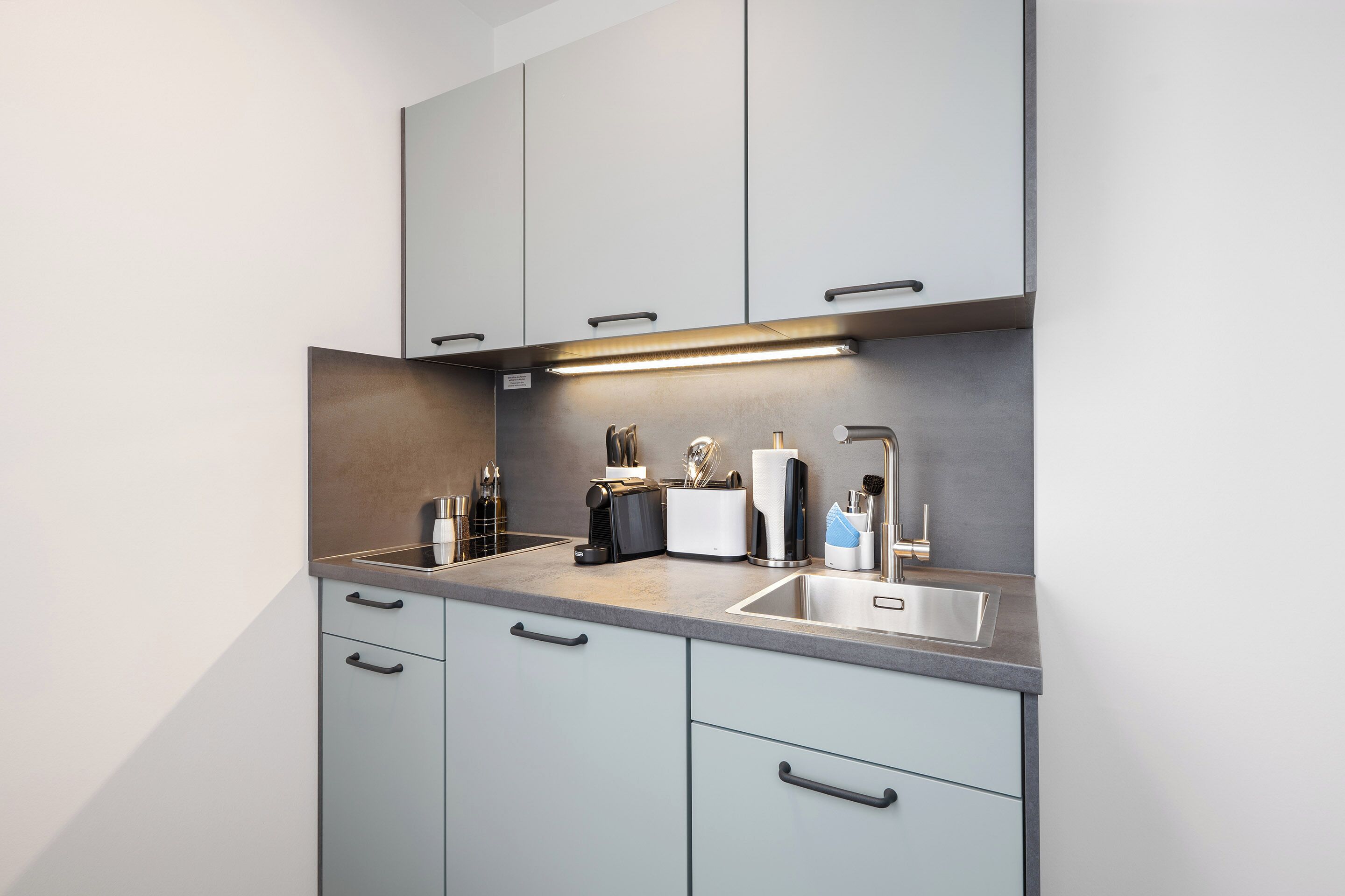 A modern kitchen with grey cabinets, a stainless steel sink, and a built-in oven.