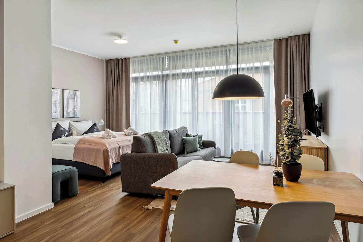 A modern hotel room with a large bed, a sofa, a dining table, and a TV.