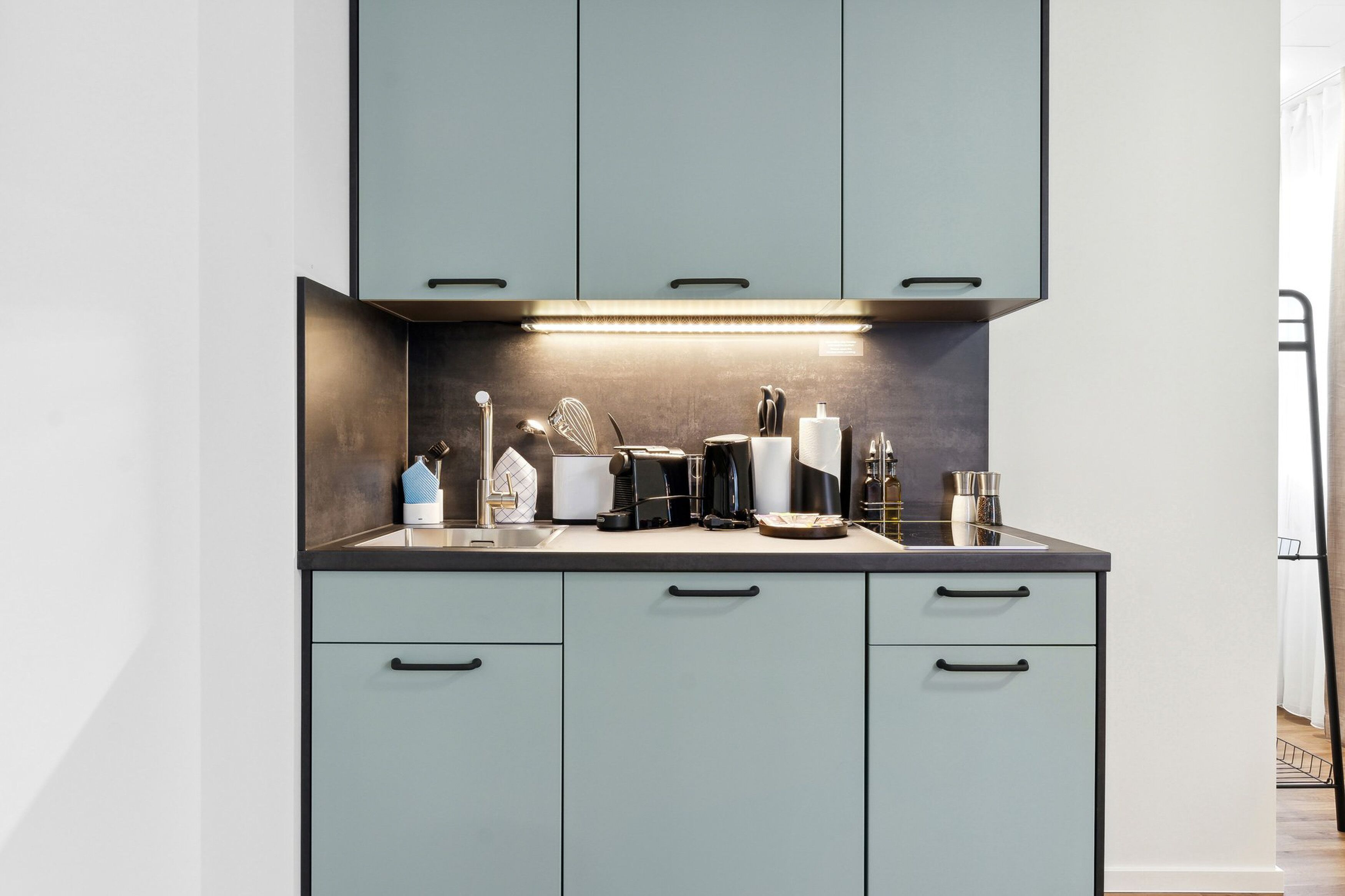 A modern kitchen with grey cabinets, a countertop with various appliances, and a backsplash.
