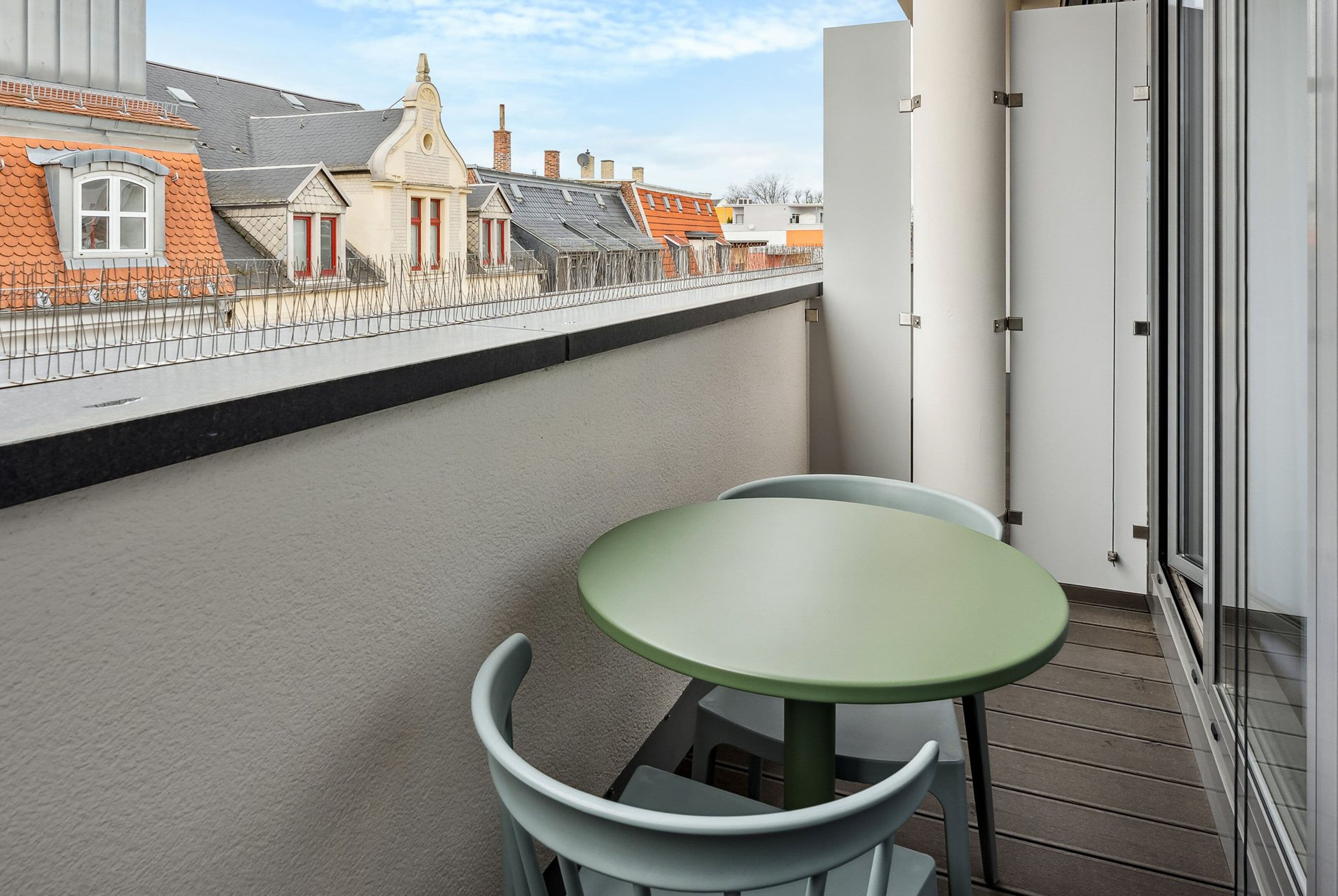 Un balcón con una pequeña mesa y sillas, con vistas a una hilera de casas de diversos estilos arquitectónicos.