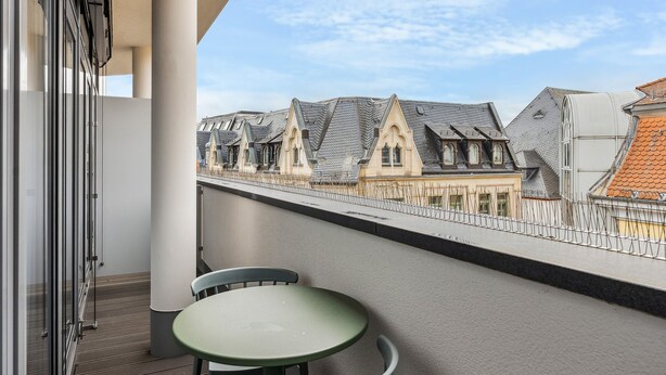 A balcony with a table and chairs, overlooking a row of traditional houses with steep roofs. - Limehome Zwickau Magazinstr. (Zwickau)