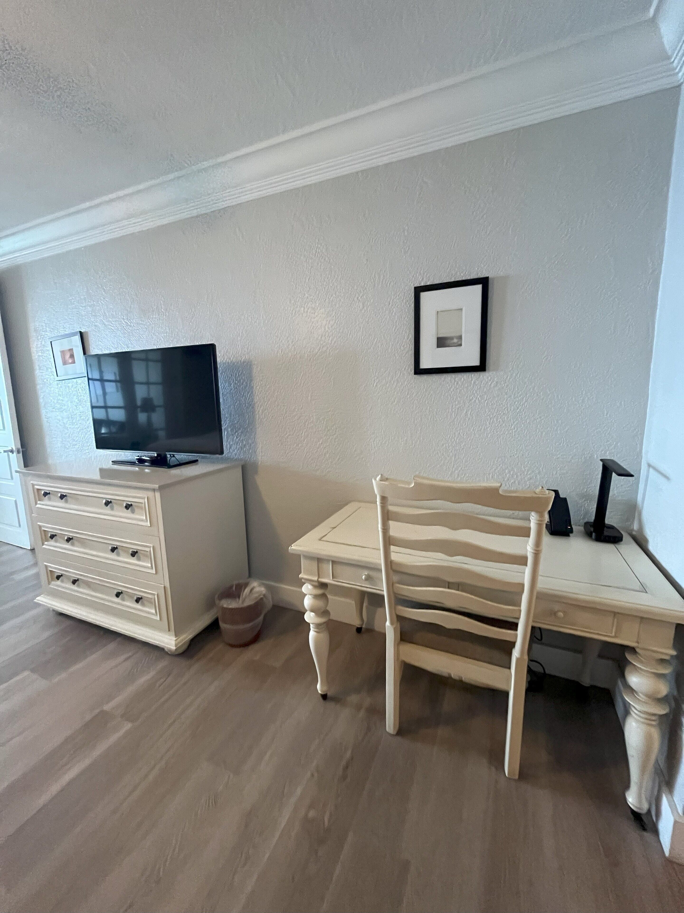 A room with a TV on a dresser, a chair, a desk, and a framed picture on the wall.