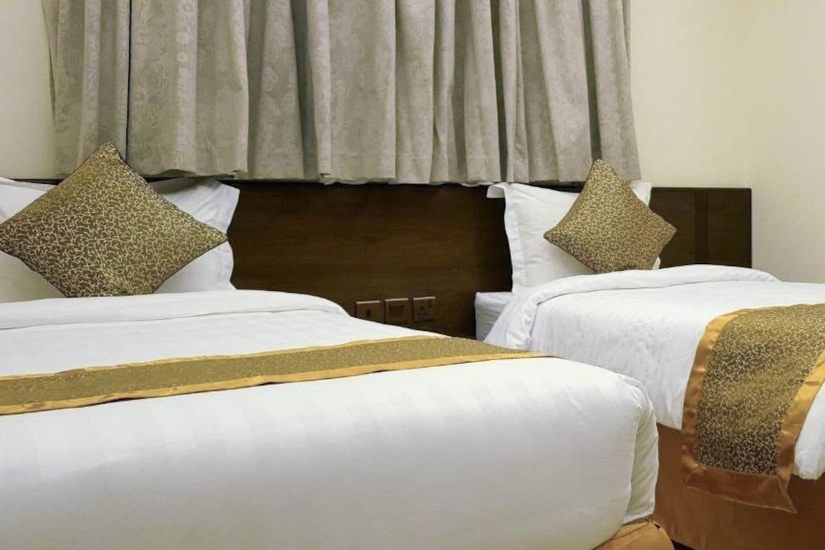 A hotel room with two beds, each with white linens and gold accents, a wooden headboard, and a painting on the wall.