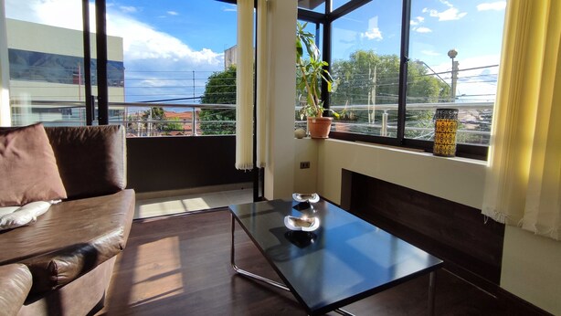 Une chambre moderne avec un canapé en cuir, une table basse en verre et de grandes fenêtres donnant sur le paysage urbain.
