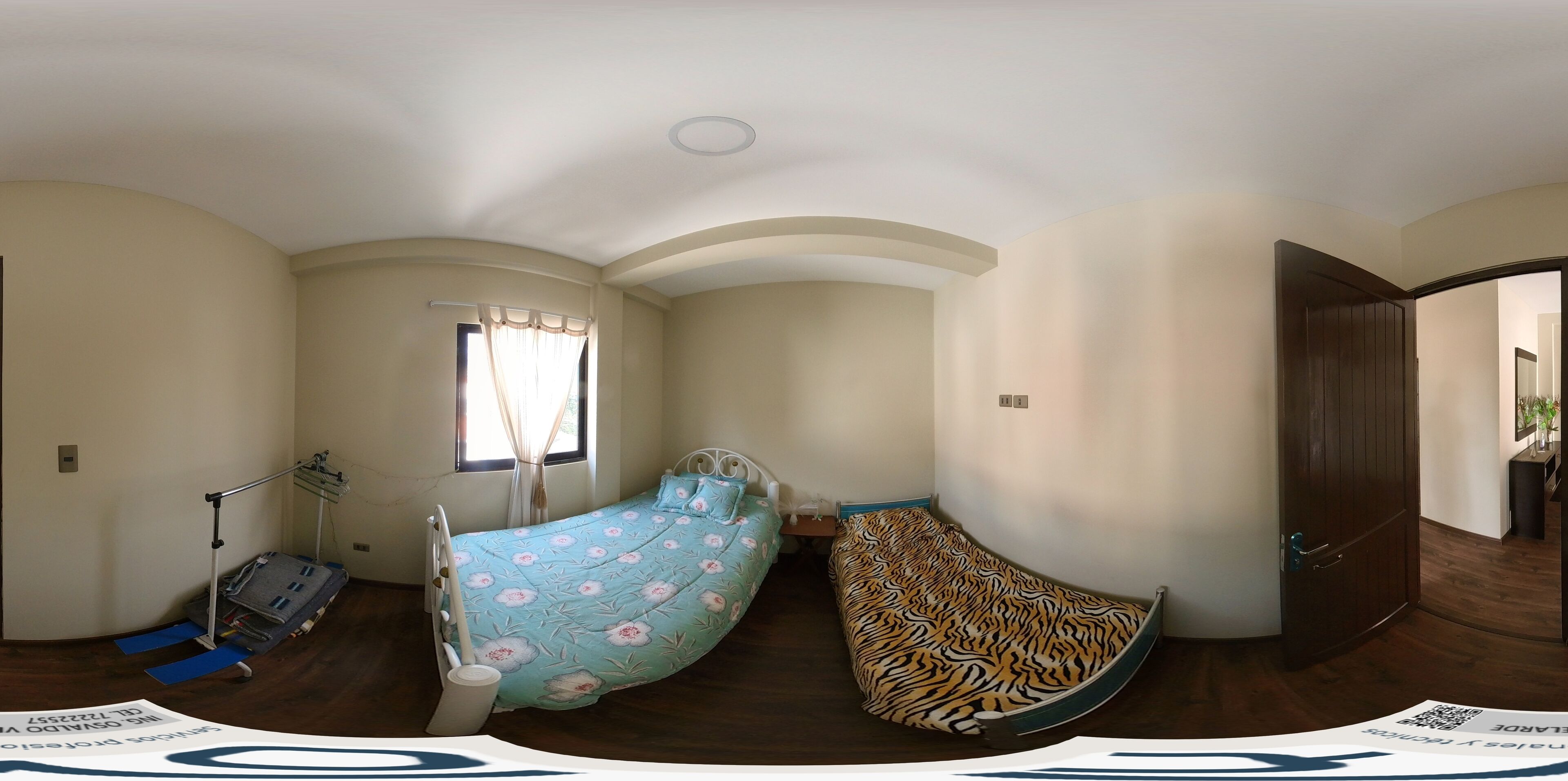 A bedroom with a curved bed, a window with curtains, a wooden floor, and a door.
