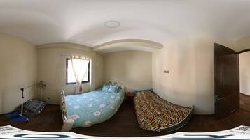 A bedroom with a curved bed, a window with curtains, a wooden floor, and a door.