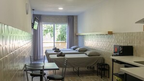 A compact hotel room with a bed, a small dining table with chairs, a kitchenette, and a view of the outdoors. - Hotel Apartamento La Ruta (Calpe)