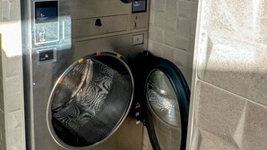 A compact, modern laundry room with two large front-loading washing machines, a control panel, and patterned floor tiles. - Hotel Apartamento La Ruta (Calpe)