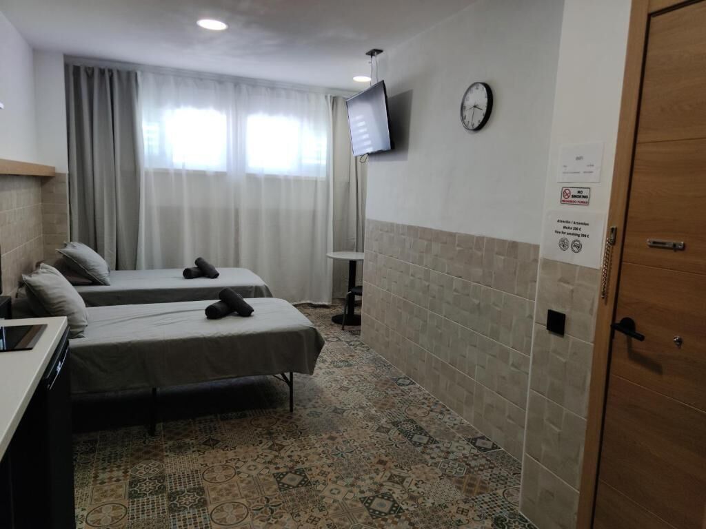Ein Hotelzimmer mit zwei Betten, einem an der Wand befestigten Fernseher, einer Uhr und einem gemusterten Boden.