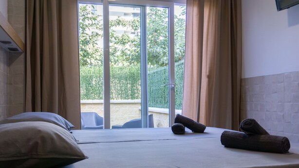 A hotel room with a bed, pillows, a towel, and a view of greenery outside. - Hotel Apartamento La Ruta (Calpe)