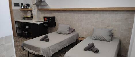 A room with two single beds, a small kitchenette, and a TV mounted on the wall.