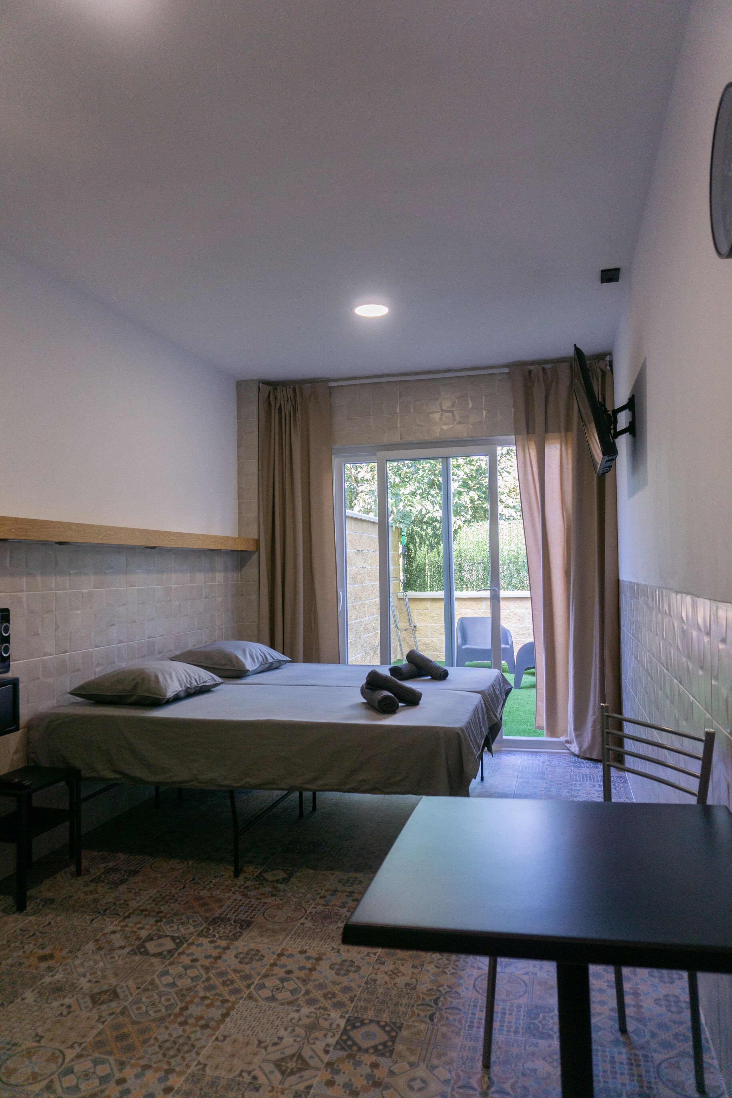A small, clean room with a bed, a table, and a window with curtains.