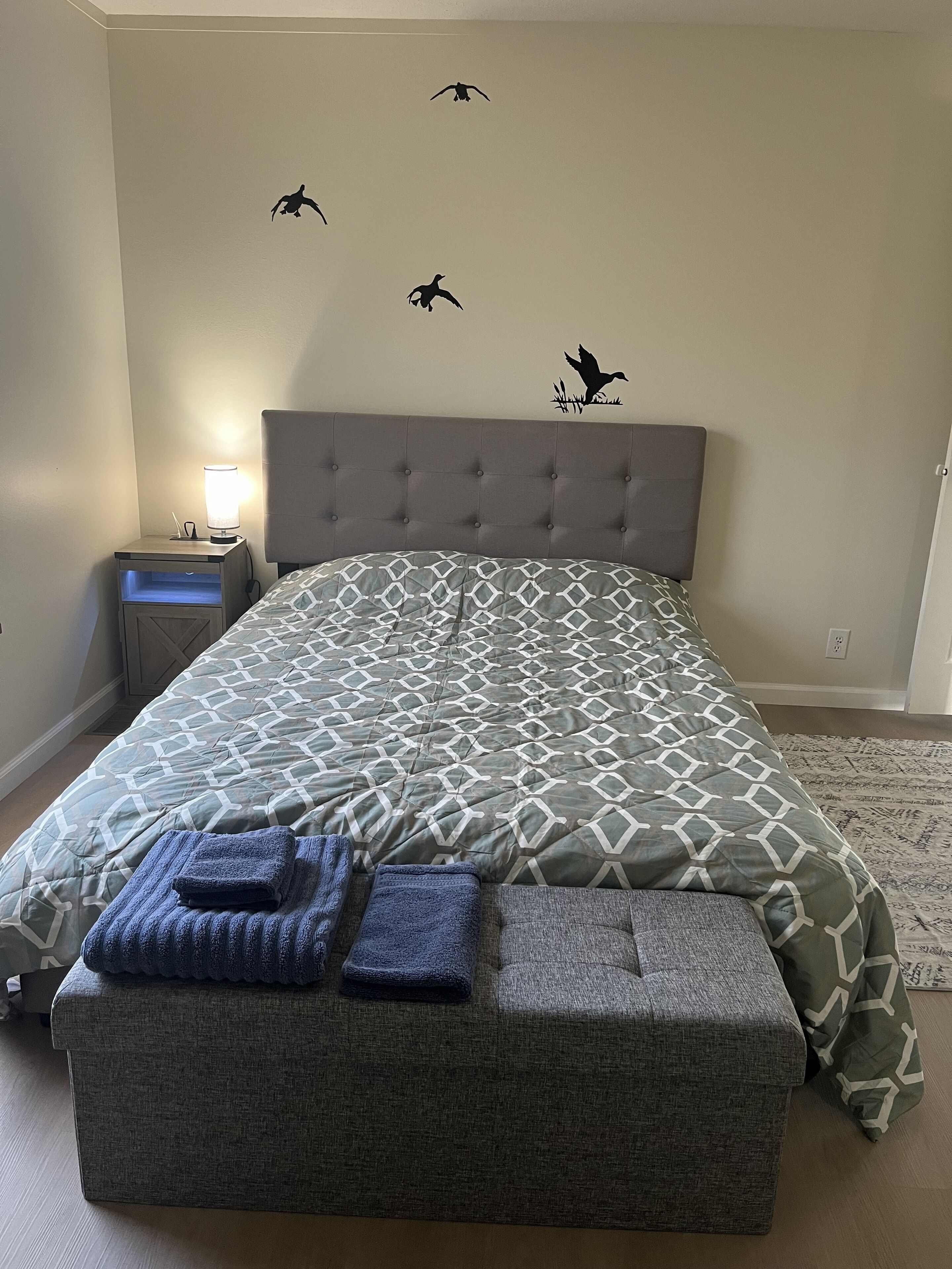 Une chambre à coucher avec un lit, une table de chevet, une lampe et des autocollants décoratifs représentant des oiseaux sur les murs.