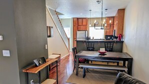 A modern kitchen with wooden cabinets, a dining area with a wooden table and chairs, and a staircase leading to another level. - Chalet 66 at the Official Collins Lake Resort (Government Camp)