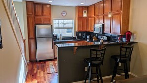 A modern kitchen with wooden cabinets, stainless steel appliances, and a central island with bar stools. - Chalet 66 at the Official Collins Lake Resort (Government Camp)