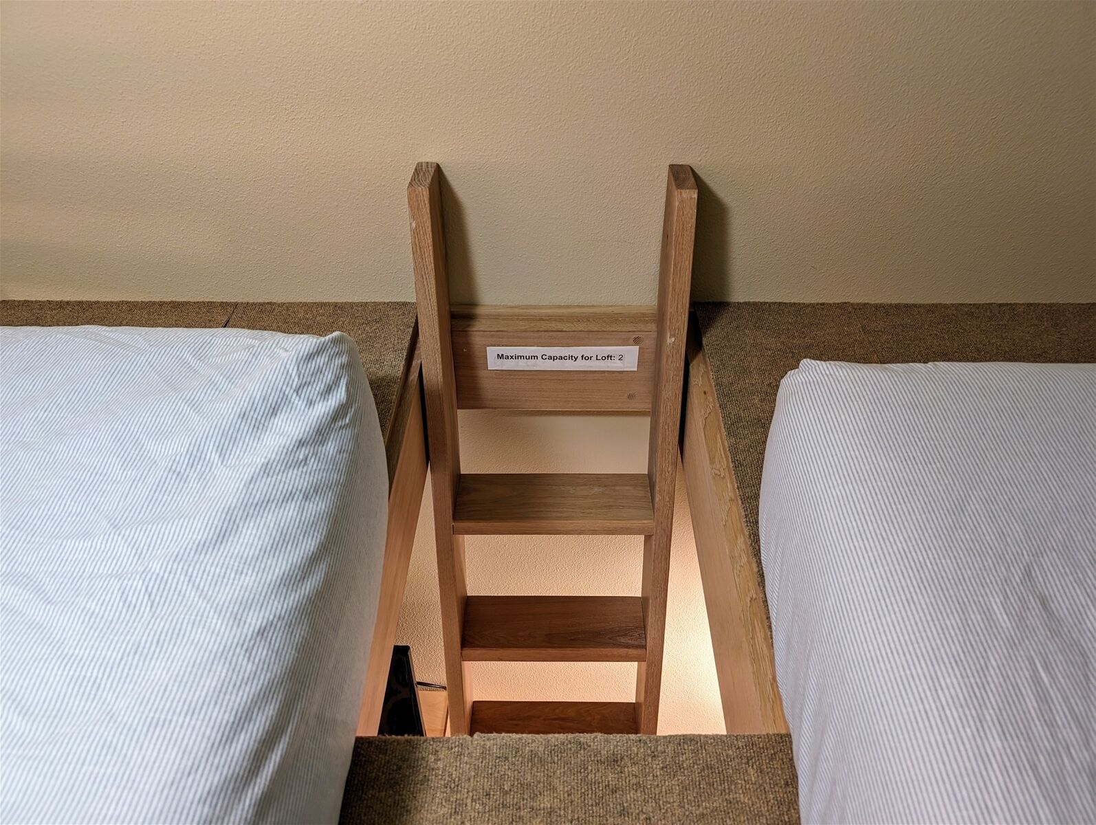 A loft bed with a wooden ladder and a label indicating a maximum capacity of 2.