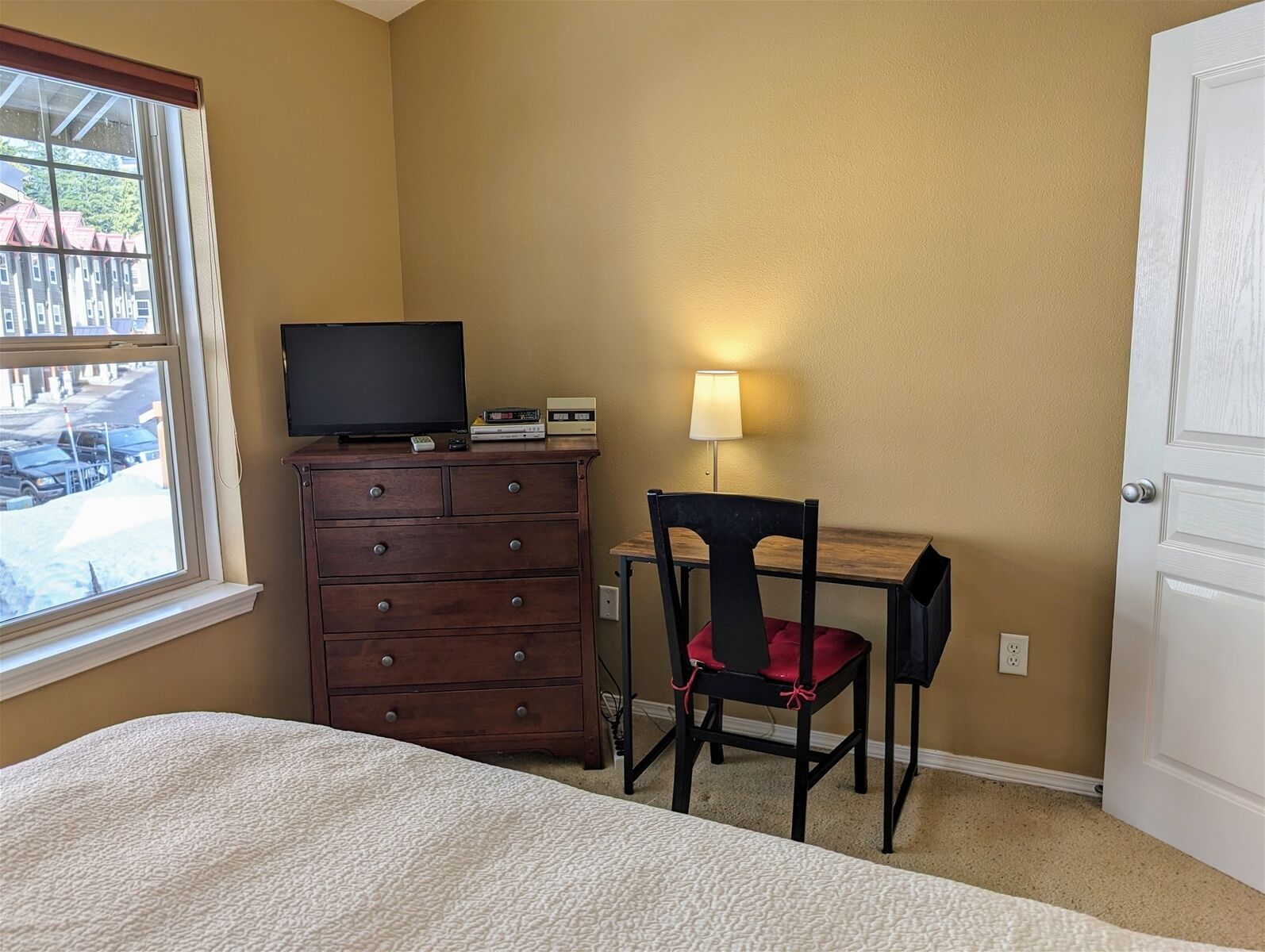 A bedroom with a bed, a dresser, a TV, a lamp, and a chair.
