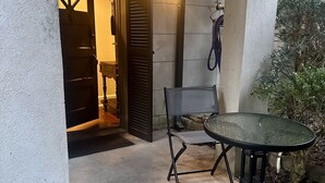 Un espace extérieur abrité avec une table et des chaises, une porte donnant sur l’intérieur et un téléphone fixé au mur.