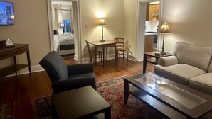 Une chambre d’hôtel comprenant un lit, une table à manger avec des chaises, un canapé et une table basse. Il y a un téléviseur accroché au mur et une lampe sur la table.