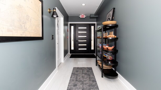 A hallway with a black door, a map on the wall, and a black shelf with various items.