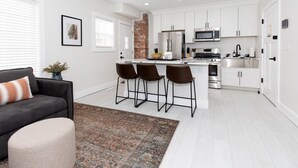 A modern kitchen with white cabinets, stainless steel appliances, and a brick accent wall.