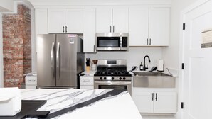 A modern kitchen with white cabinets, stainless steel appliances, and a marble countertop.