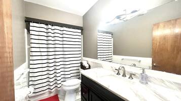 A bathroom with a striped shower curtain, a toilet, a sink with a mirror, and a red bath mat.