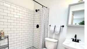 Ein Badezimmer mit weiß geflißter Dusche, Toilette, Waschbecken und Spiegel.