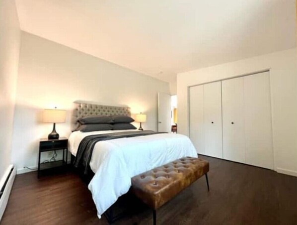 Un dormitorio con cama, mesitas de noche, un banco y un armario.
