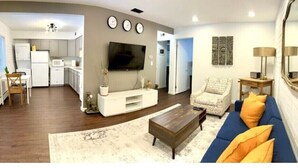 A modern living room with a sofa, coffee table, and a television. There is a kitchen area visible in the background. - Stylish 2BR in Historic WaterHill / Walk to Downtown & The Big House (Ann Arbor)