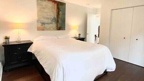 A bedroom with a bed, a nightstand, a lamp, a painting, and a wardrobe. - Stylish 2BR in Historic WaterHill / Walk to Downtown & The Big House (Ann Arbor)