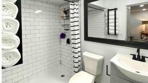 A modern bathroom with a white tiled shower, a toilet, and a sink with a large mirror. - Stylish 2BR in Historic WaterHill / Walk to Downtown & The Big House (Ann Arbor)
