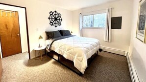 A bedroom with a bed, a bedside table, a wall decoration, a window, and a door.