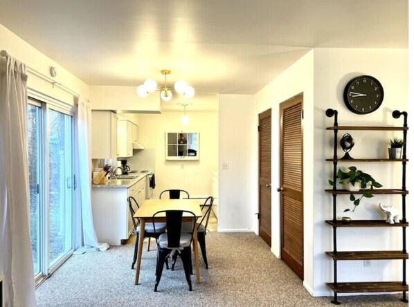 A compact kitchen with a dining area, a clock on the wall, and a plant shelf.