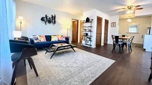 A living room with a sofa, coffee table, and a rug. There is a dining area with a table and chairs.