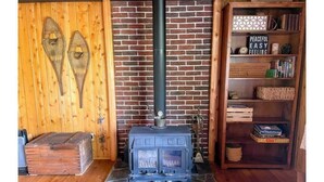 A rustic room with a brick wall, a wooden floor, a stone hearth, a vintage stove, and a bookshelf with various items.